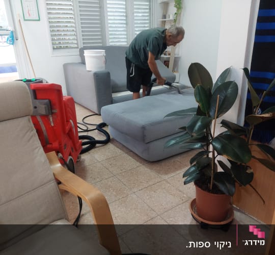 אדם מנקה ספה עם שואב אבק מקצועי